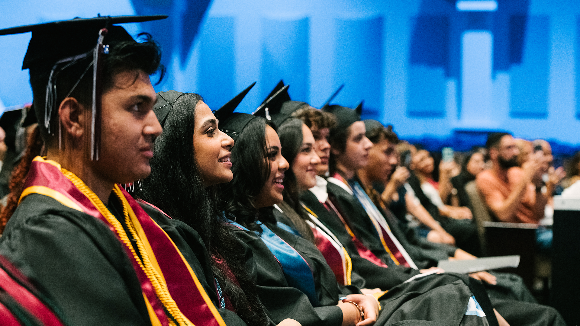 Students wearing graduation attire sit in an auditorium during their commencement.